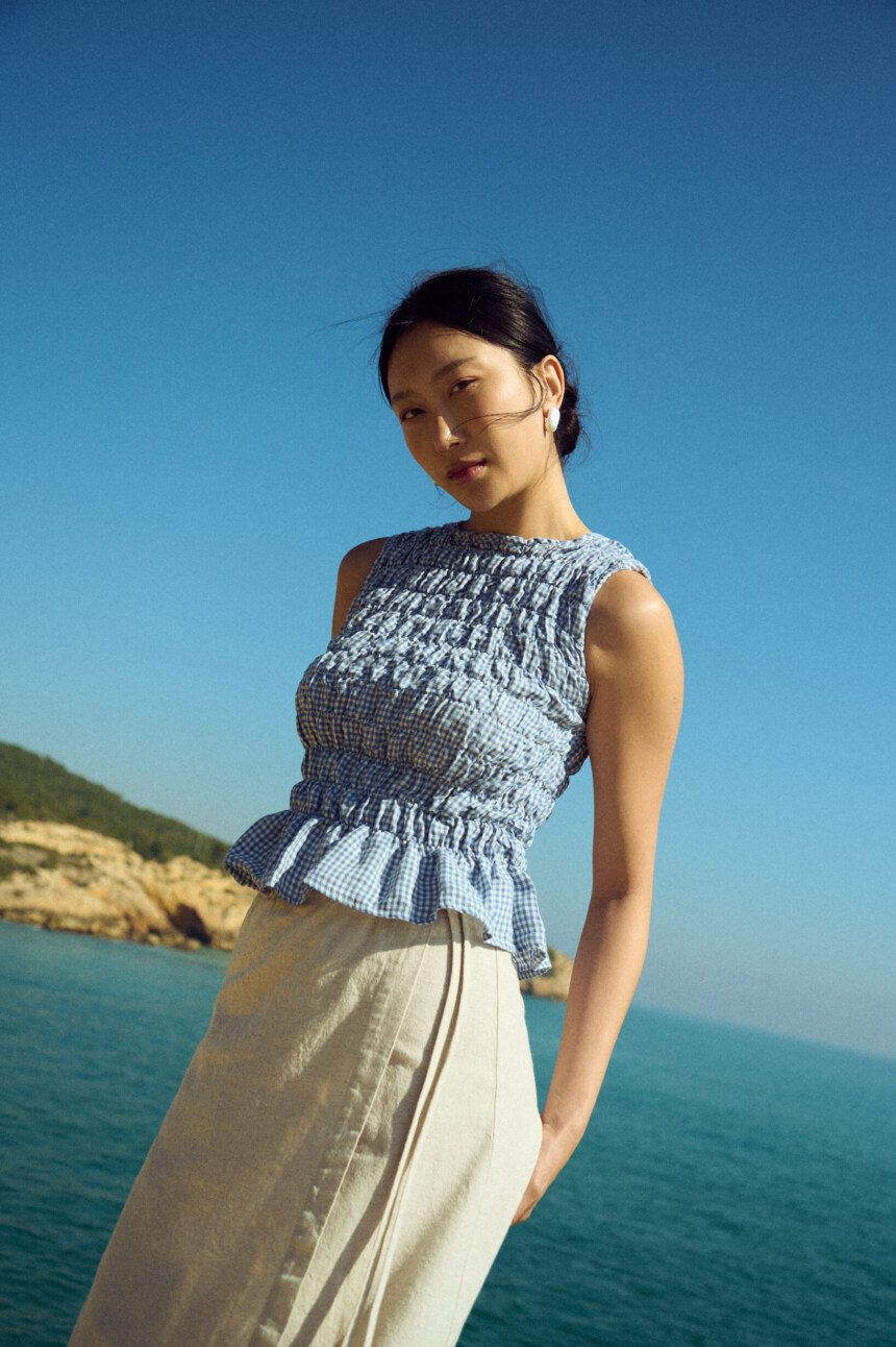 Blue gingham linen smocked top with gathered texture and soft peplum hem, paired with a natural linen cotton blend wrap skirt