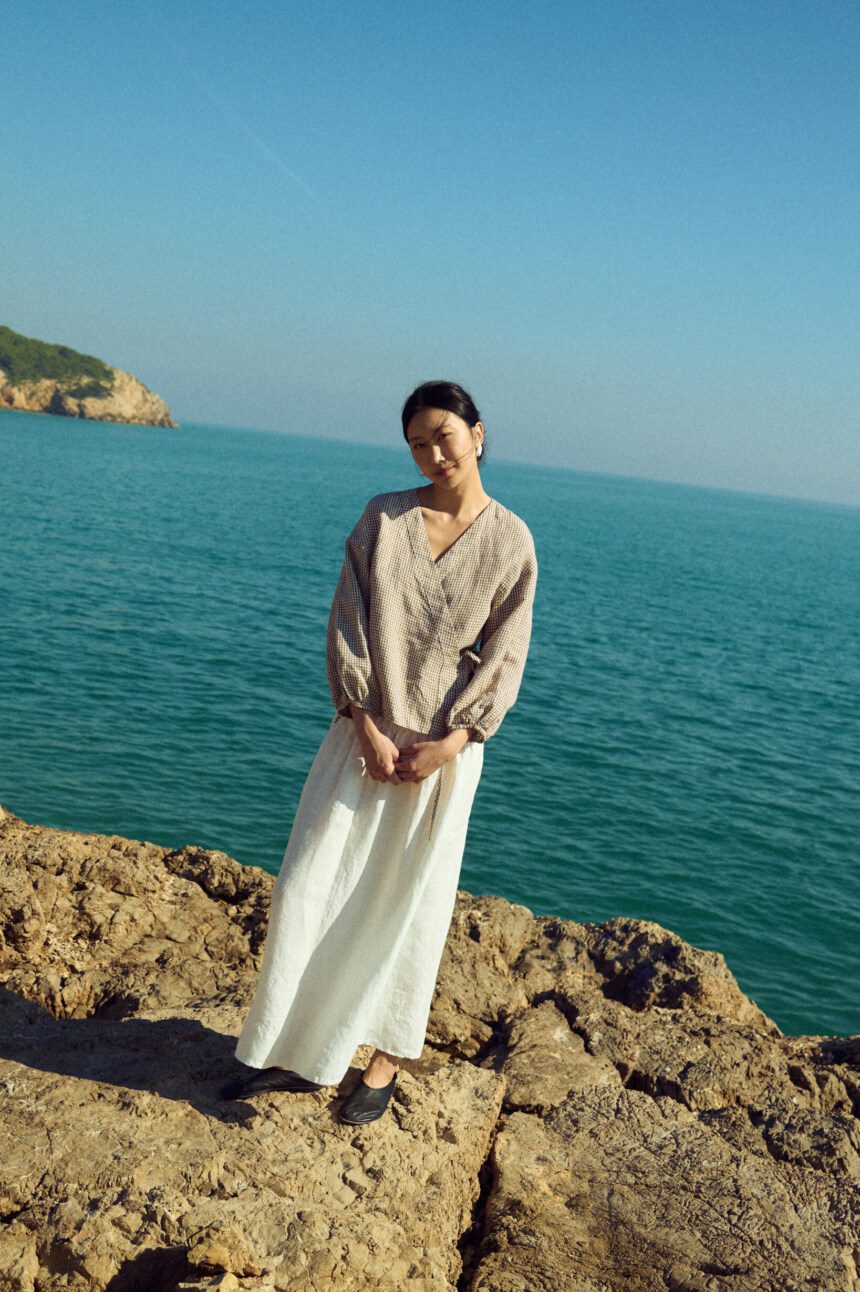 Brown gingham linen wrap top with soft V neckline and adjustable side tie, paired with a white linen skirt