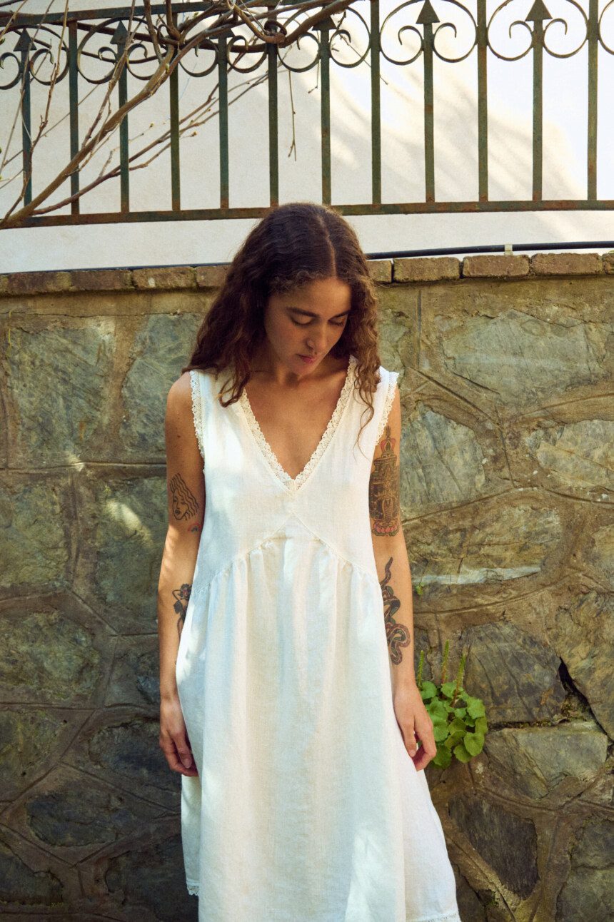 Close front view of milky white linen sleeveless midi dress with V-neck, lace-trim neckline, and softly gathered waist
