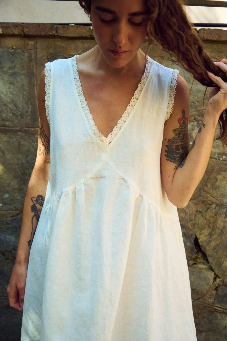 Detail view of milky white linen sleeveless midi dress with lace-trim V-neck and armholes, gathered waist seam, and soft texture