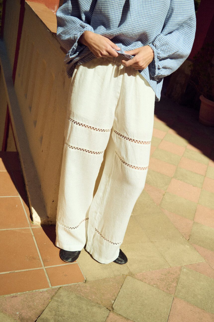Wide-leg white linen trousers with horizontal lace insets, soft elastic waistband, and an easy, fluid drape