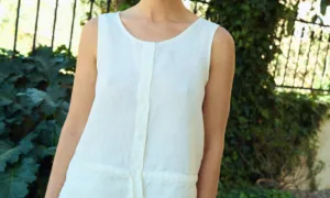 White sleeveless linen top with a relaxed fit, round neckline, button-front closure, and subtle waist seam with tie detail
