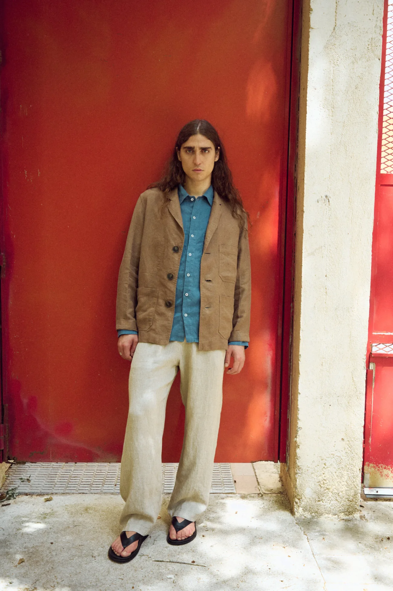 Men’s brown heavy linen jacket with a relaxed blazer-inspired fit, notched lapels, three-button front and roomy patch pockets, layered over a stellar blue linen shirt and loose natural grey linen trousers