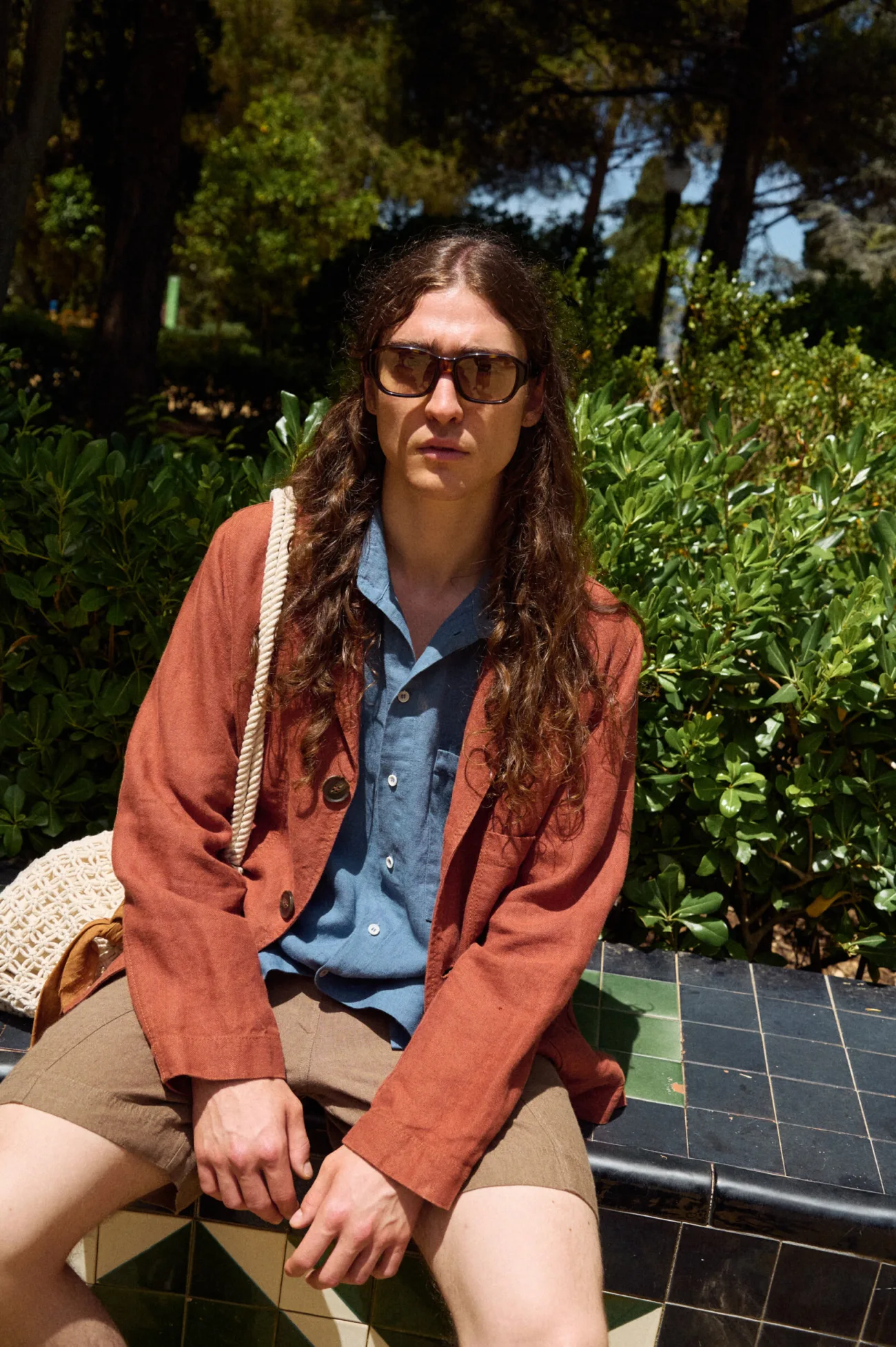 Men’s terracotta heavy linen jacket with a laid-back blazer shape, notched lapels, dark buttons and practical patch pockets, styled with a stellar blue linen shirt and relaxed brown linen shorts