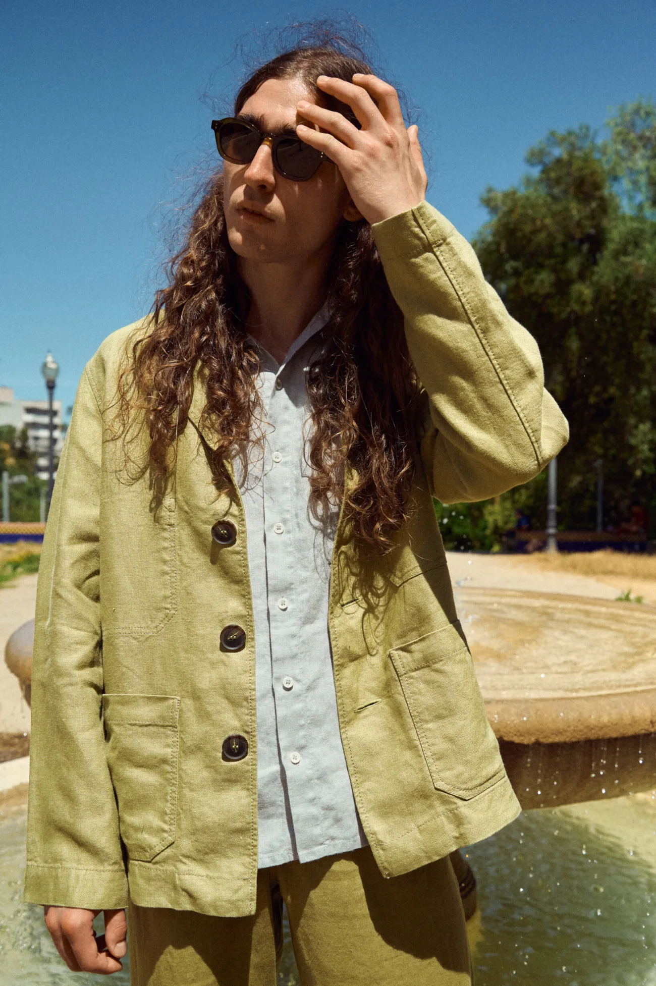 Olive heavy linen jacket for men, cut in a laid-back tailored shape with classic lapels, oversized dark buttons and practical patch pockets, worn with an ice grey linen shirt and coordinating olive trousers