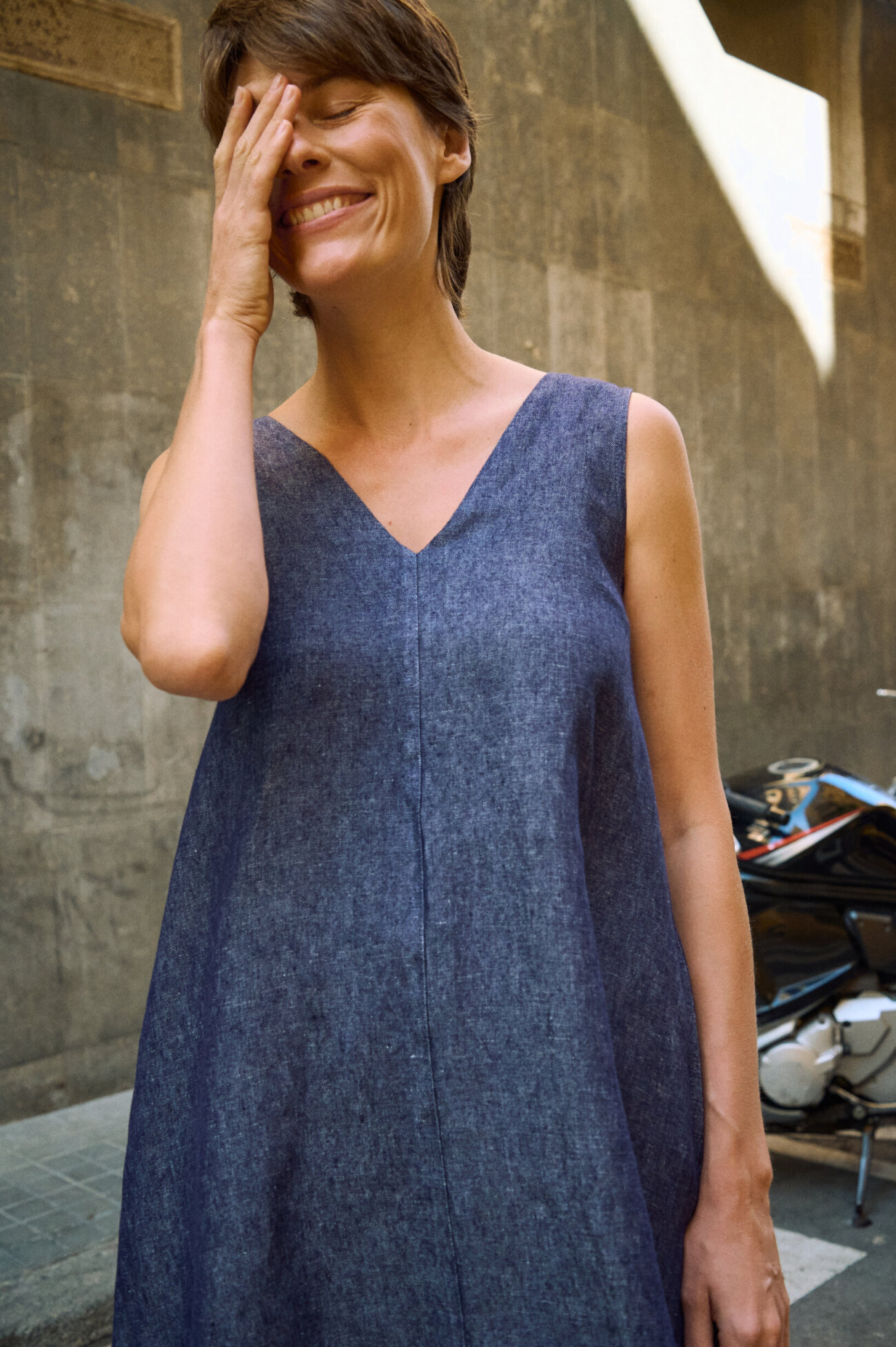 Close-up of a sleeveless blue denim linen maxi dress with a V-neckline, relaxed A-line silhouette and visible center seam
