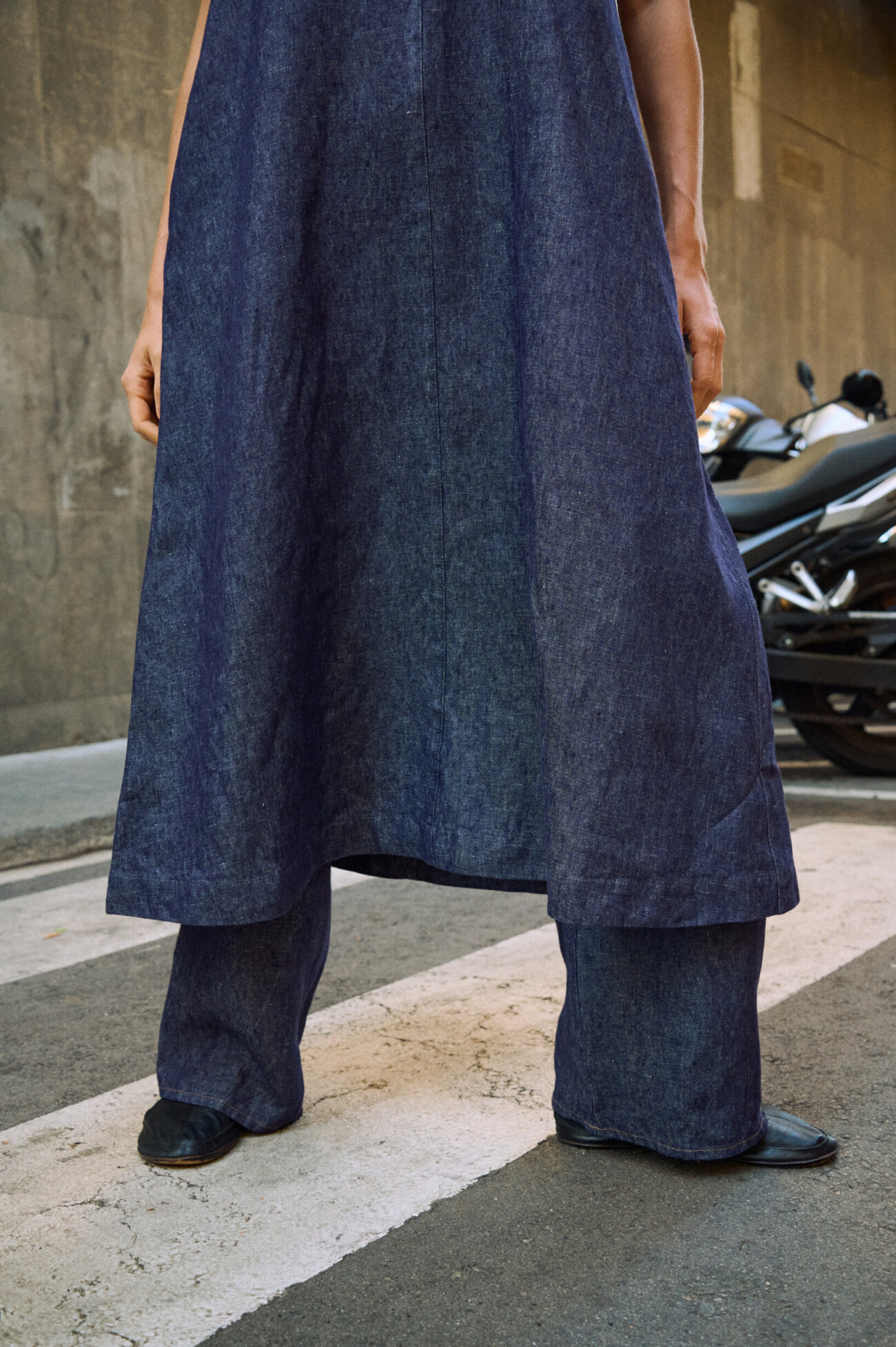 Close-up of a blue denim linen sleeveless maxi dress layered over matching wide-leg linen pants, highlighting the natural linen texture and flowing hem