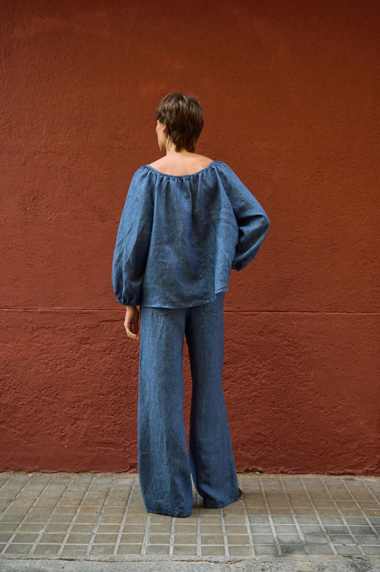 Rear view of blue striped linen wide-leg pants styled with a matching relaxed blouse with voluminous sleeves
