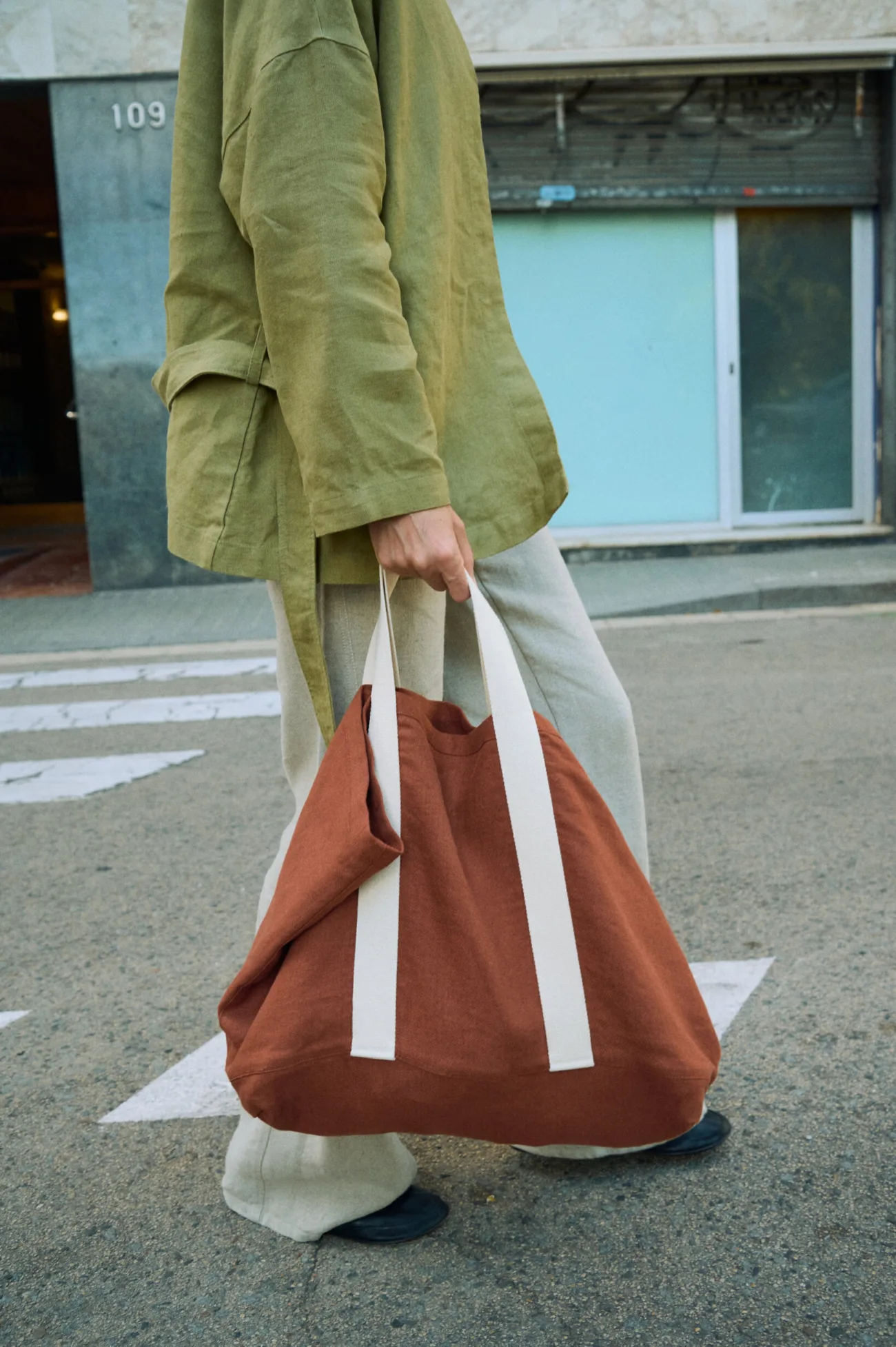 Terracotta heavy linen tote bag with wide cotton handles, shown carried by hand