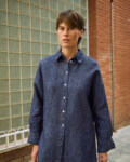 Front detail of blue denim linen shirt with button-down front, pointed collar, dropped shoulders, and wide cuffs