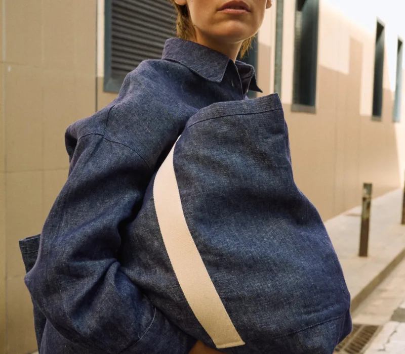 Denim linen tote bag with wide cream cotton handles, shown carried with a matching denim linen shirt