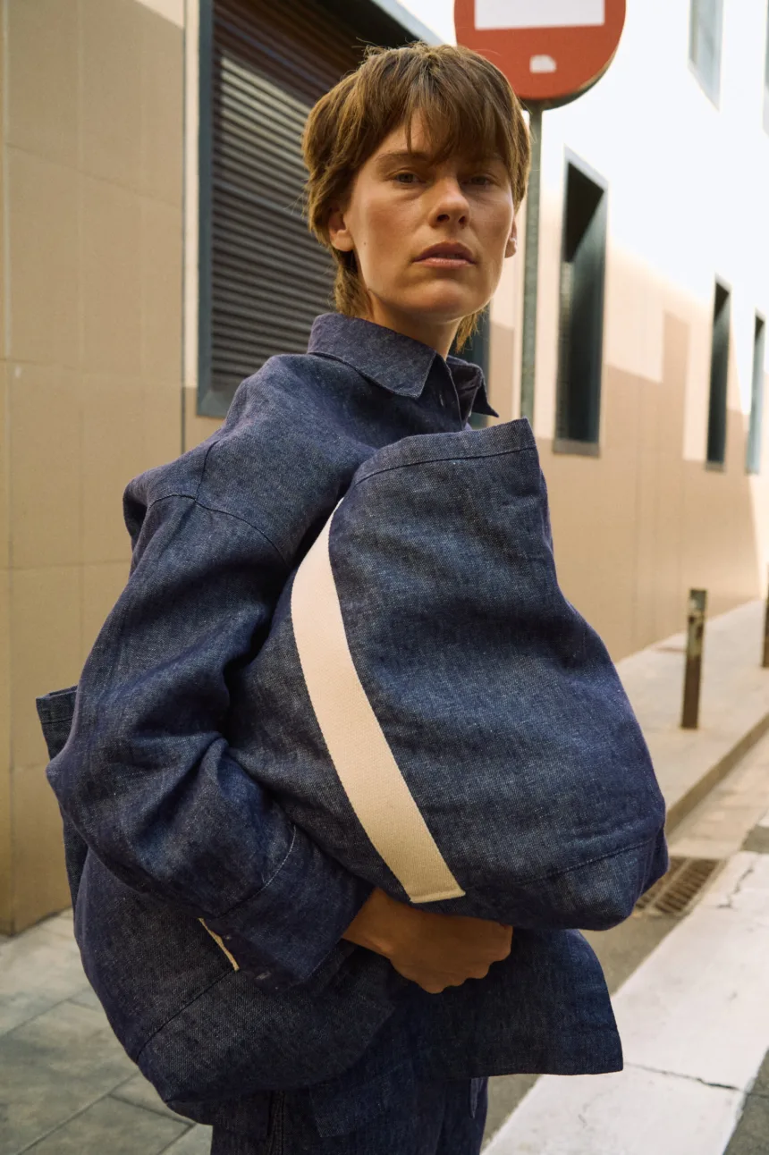 Denim linen tote bag with wide cream cotton handles, shown carried with a matching denim linen shirt