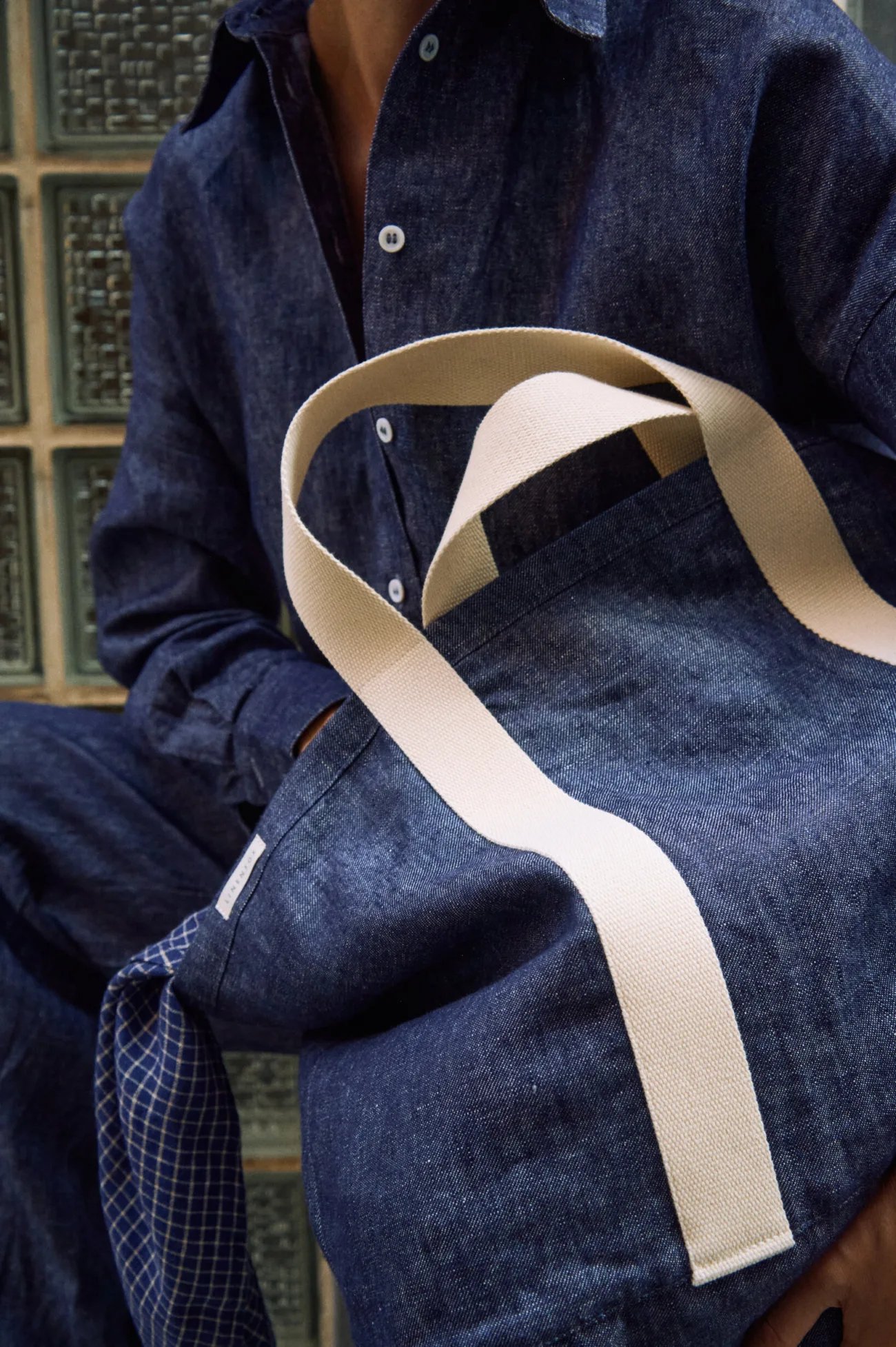 Close-up of a denim linen tote bag with wide cream cotton handles, styled with a matching denim linen button-up shirt