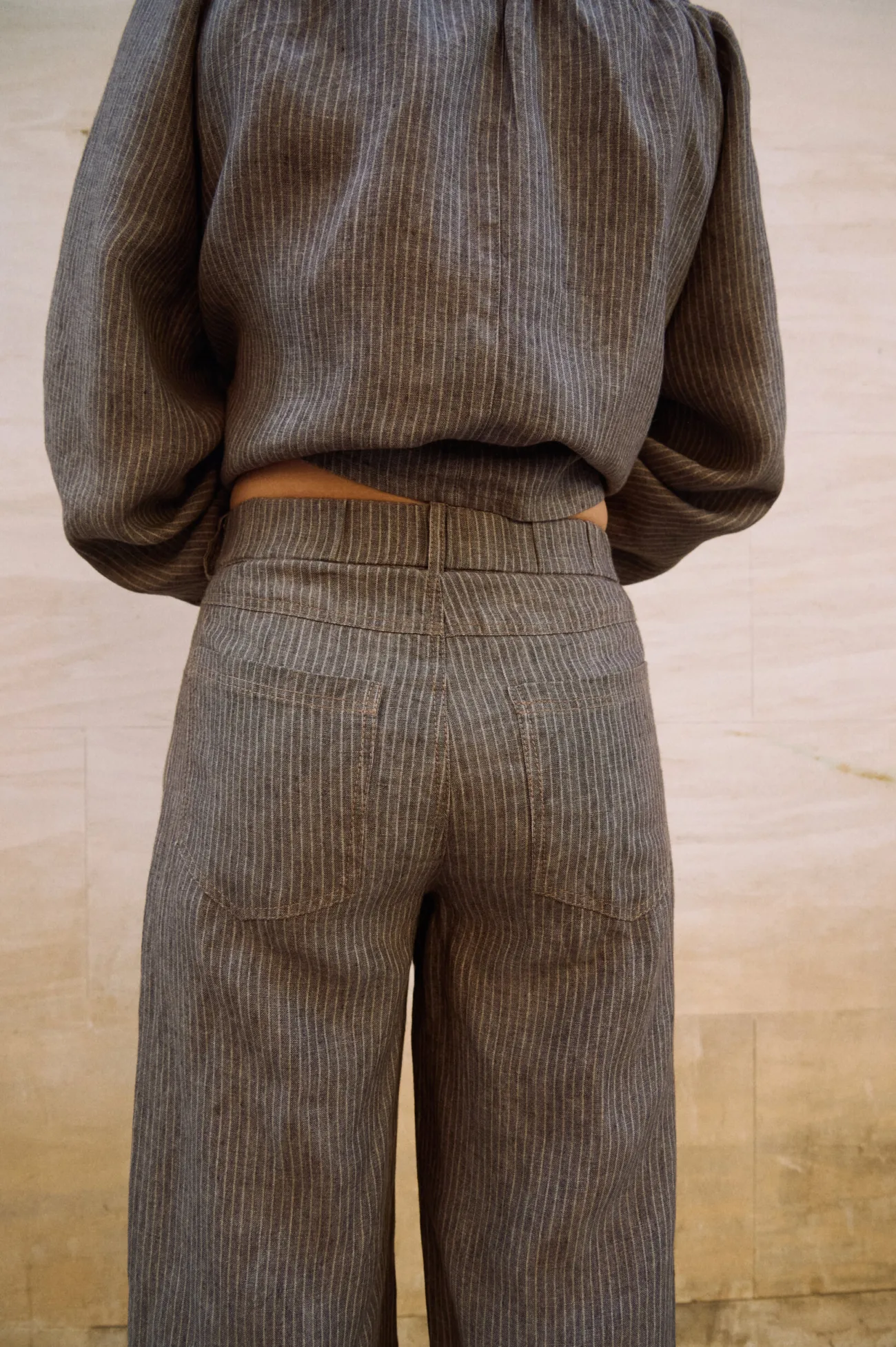 Close-up back view of brown striped linen wide-leg trousers with patch pockets and a structured waistband