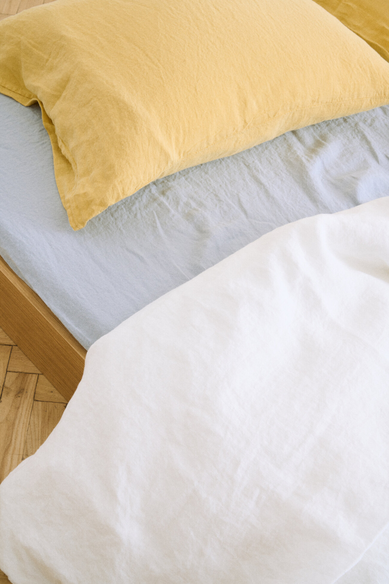 White linen duvet cover layered with soft blue linen bedding and a butter yellow pillowcase